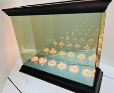 many lit candles are placed in a glass case on the floor next to each other