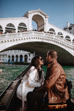 a man and woman sitting in a boat on the water near a bridge with gondola