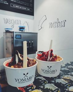 two ice cream bowls filled with different types of toppings on top of a table