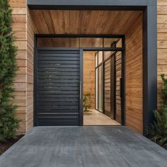 an entrance to a modern home with wood siding and black steel doors, surrounded by greenery