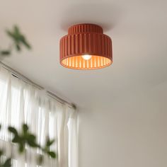 an orange light hanging from the ceiling in a room with white curtains and window coverings