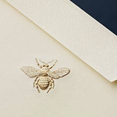 a gold bee brooch sitting on top of a white piece of paper next to a blue and white wall