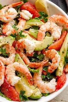 a white bowl filled with shrimp, avocado and tomato salad on top of a table