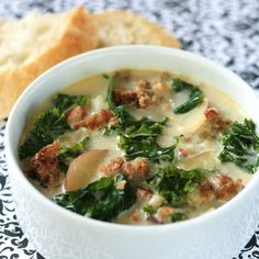 a bowl of soup with meat and spinach in it next to a roll on a table