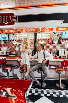 a man and woman sitting in front of a hot dog stand with red chairs around them