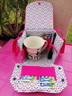 a pink table topped with a cup and some kind of case on top of it