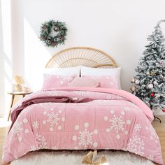 a pink bed with white snowflakes on it and a christmas tree in the corner