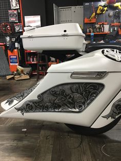 a white motorcycle parked in a garage next to a boat on the floor with other tools behind it