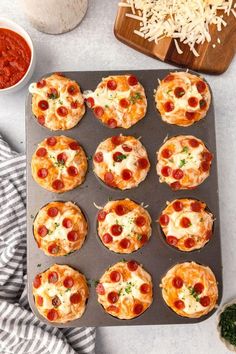 mini pizzas with cheese and pepperoni on a baking sheet next to some parmesan cheese