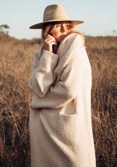 a woman in a white coat and hat is standing in the middle of a field