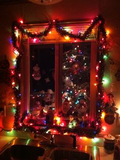 a kitchen decorated for christmas with lights on the windowsill and decorations around the window