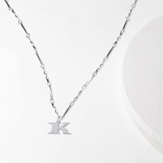 We've transformed the font used on U.S. currency into letter necklaces, so that you can channel in your own personal fortune. The letter K charm is embellished with subtle black enamel detailing along the side and our signature wave design on the back. The twisted bar chain is adjustable so you can wear it as a choker or everyday pendant. These initial necklaces are intended as a form of self expression for you or the Ks in your life. Charm Dimensions: ~12mm / 0.5" (h) Chain Length: 16"-20" adju Dainty Silver Initial Pendant Chain Necklace, Dainty Silver Chain Necklace With Initial Pendant, Trendy Initial Pendant Necklace, Trendy Silver Initial Pendant Necklace, Silver Initial Necklace With Adjustable Clavicle Chain, Trendy Silver Initial Necklace With Clavicle Chain, Adjustable Silver Initial Necklace With Clavicle Chain, Silver Necklace With Initial Pendant And Paperclip Chain, Trendy Silver Initial Necklace With Adjustable Chain