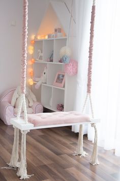 a white swing bed with pink pillows and lights hanging from it's sides in a child's room