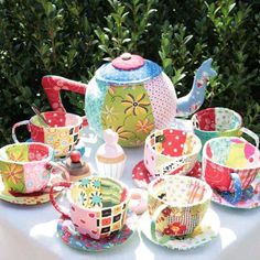 a table topped with cups and saucers covered in colorful designs next to shrubbery