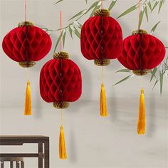 four red paper lanterns hanging from a bamboo tree with yellow tassels on them