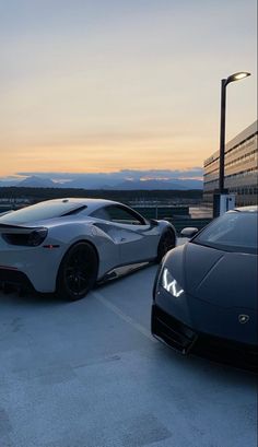 two sports cars parked next to each other in a parking lot at dusk with mountains in the background