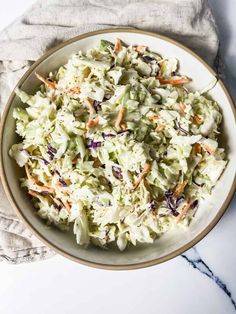 a white bowl filled with coleslaw salad on top of a marble countertop