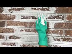 a person with green gloves on their hands is holding something up against a brick wall