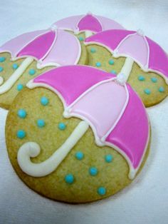 decorated cookies with pink and blue umbrellas on white tablecloth, ready to be eaten