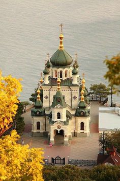 an ornate building with gold and green roofing near the water in front of some trees