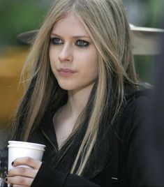 a woman holding a coffee cup and looking at the camera while wearing a black jacket