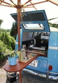 an old blue van with its trunk open and flowers in the back seat under it