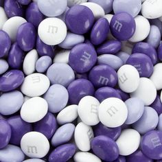 purple and white m & m's with the letter m on them are scattered together