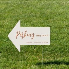 a white sign that says parking this way on it in the middle of some grass