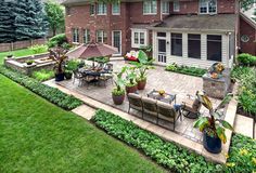 an outdoor patio with tables and chairs in front of a large brick house surrounded by greenery