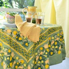 a table covered in yellow and green cloths with lemons on it, next to a potted plant