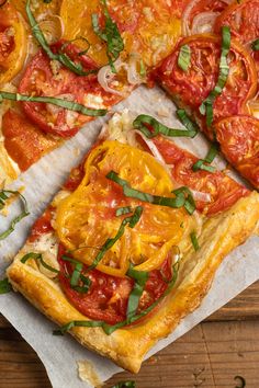 a pizza with tomatoes, cheese and herbs on it sitting on top of a piece of parchment paper