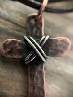 "Show your faith with this humble, rustic cross. I hammer and forge each of these crosses by hand from pure, organic copper and wrap it with 925 Sterling silver. Each cross is finished with a rustic patina which gives it an antiqued look. These are perfect for men or women. Dark brown cowhide leather cording is 24\" in length and is adjustable. Necklace slips over the head. If you would like another style chain like a ball chain or cable chain please message me before ordering. Prices may vary b Artisan Adjustable Cross Jewelry, Rustic Cross Jewelry For Gifts, Rustic Cross Jewelry Gift, Rustic Brown Hammered Jewelry, Artisan Brown Cross Jewelry, Handmade Brown Cross Jewelry, Adjustable Brown Cross Necklace, Handmade Adjustable Cross Necklace, Rustic Cross