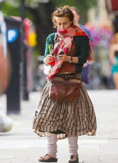 a woman walking down the street while looking at her cell phone and wearing a scarf