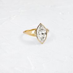 a yellow gold ring with a pear shaped diamond in the center on a white surface