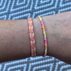 a person's arm with two different colored bracelets on it and one is wearing a pink, yellow, and orange braided bracelet