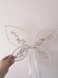 a hand holding a white butterfly shaped object with flowers on it's back and wings