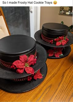 two black plates topped with poinsettis on top of a wooden table next to a window