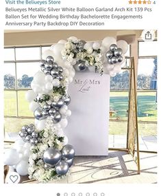 the balloon arch is decorated with silver and white balloons, greenery, and flowers