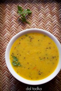 a white bowl filled with soup sitting on top of a woven table cloth next to a green leafy garnish