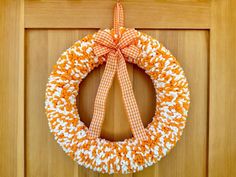 an orange and white wreath hanging on a wooden door with a ribbon tied around it