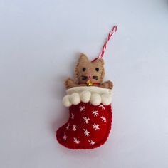 a teddy bear in a christmas stocking ornament hanging from a string on a white surface