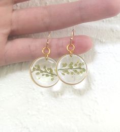 a pair of earrings with leaves painted on the glass and gold plated earwires