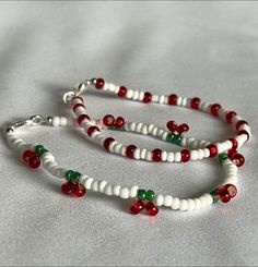 two white and red beaded bracelets with bells on each strand, sitting on a bed