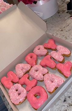 a box filled with pink frosted donuts sitting on top of a counter next to cupcakes