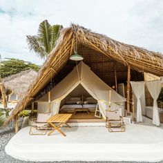 two lawn chairs sitting under a thatched roof next to a bed in the sand