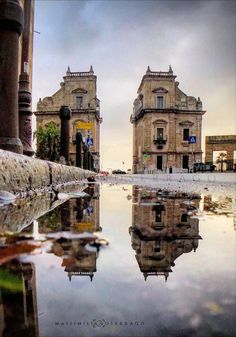 the reflection of two buildings is shown in the wet surface of the water on the street