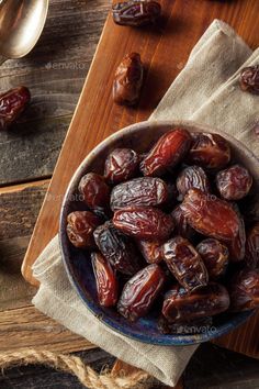 a bowl filled with dates sitting on top of a wooden table next to spoons