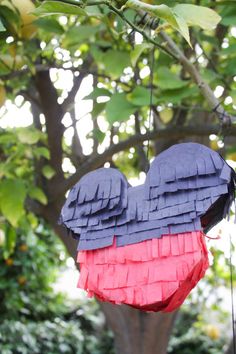 a red, white and blue paper bird hanging from a tree with green leaves in the background