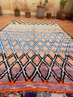 a multicolored rug on the ground with potted plants in the background