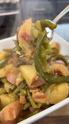 a spoon full of food with potatoes and green beans in it, being held by someone